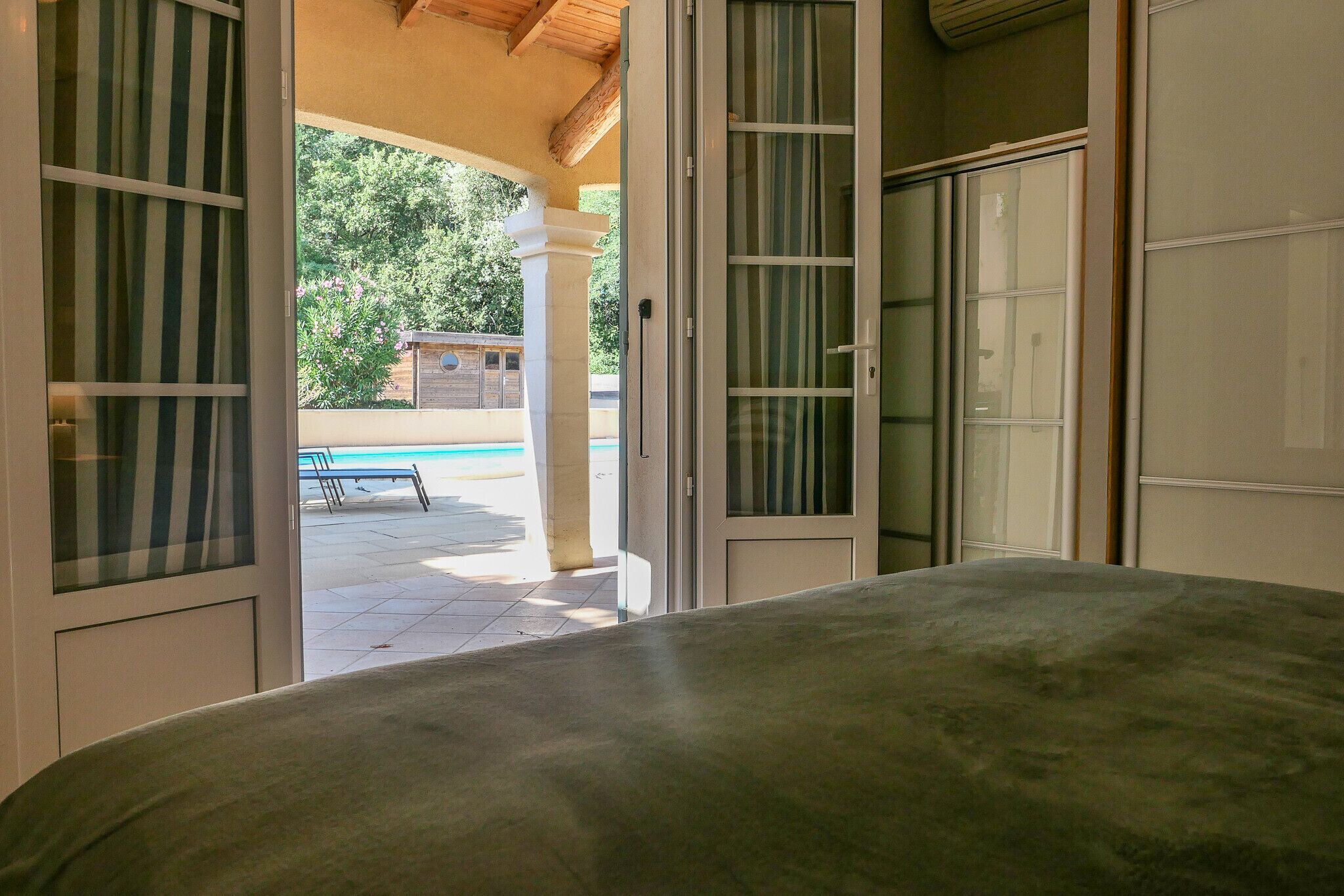 A room with a bed, a sliding glass door leading to an outdoor area with a pool and lounge chairs.