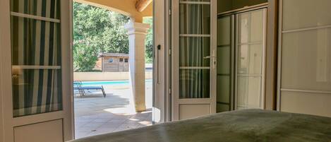 A room with a bed, a sliding glass door leading to an outdoor area with a pool and lounge chairs.
