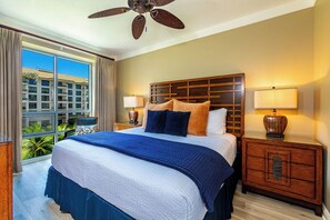 Une chambre d’hôtel avec un grand lit, un ventilateur de plafond, une table de chevet avec une lampe et une vue sur un immeuble par la fenêtre.