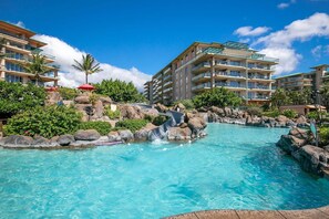 Une piscine de complexe hôtelier avec un toboggan aquatique, entourée d’immeubles à plusieurs étages dotés de balcons et d’une végétation luxuriante.