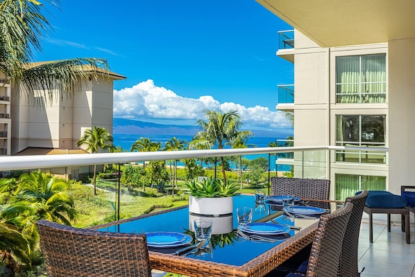 Ein Balkon mit Glastisch, gedeckt für ein Essen, mit Blick auf einen Pool und üppiges Grün.