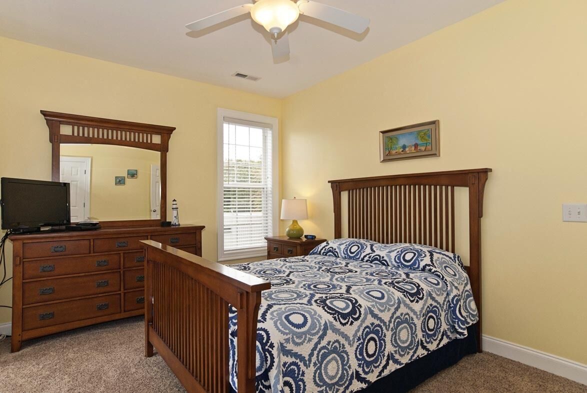Une chambre à coucher avec un lit, une commode, un miroir et un ventilateur de plafond.