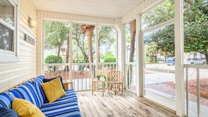 A covered porch with a blue-striped sofa, two chairs, and a view of the street. - Private Pool ~ Porch ~ Fire Pit ~ Pet Friendly (Destin)