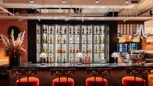 A bar area with a wine and liquor display, red cushioned bar stools, and a decorative plant. - Second Nature London Chiswick (London)