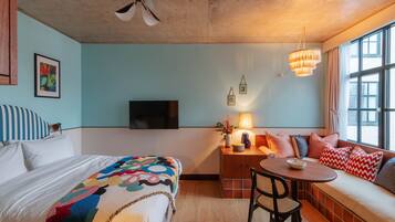 Quarto com cama, escrivaninha, cadeira, sofá, televisão e janela com cortinas.