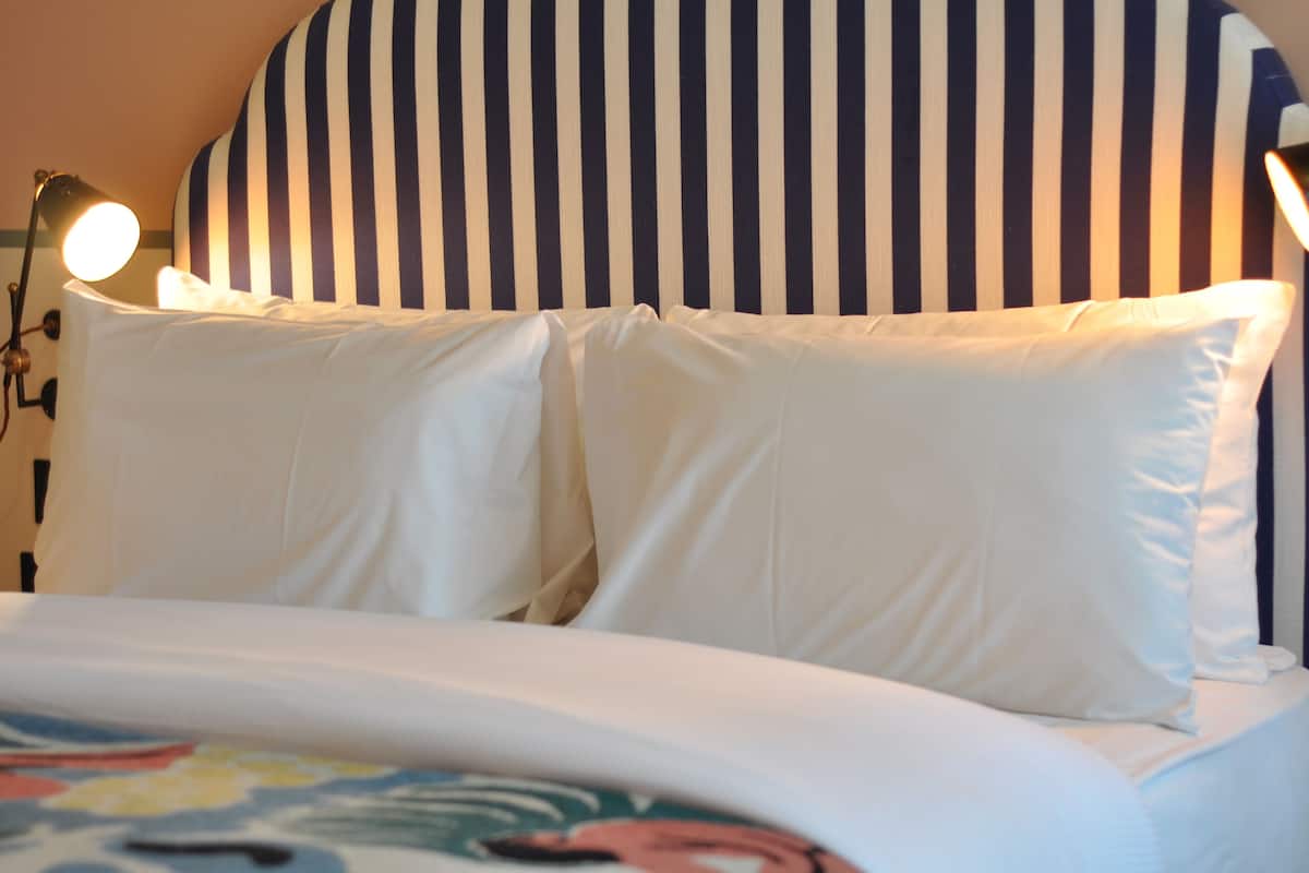 A bed with white linens and striped headboard, two bedside lamps, and a partial view of a colorful bedspread.
