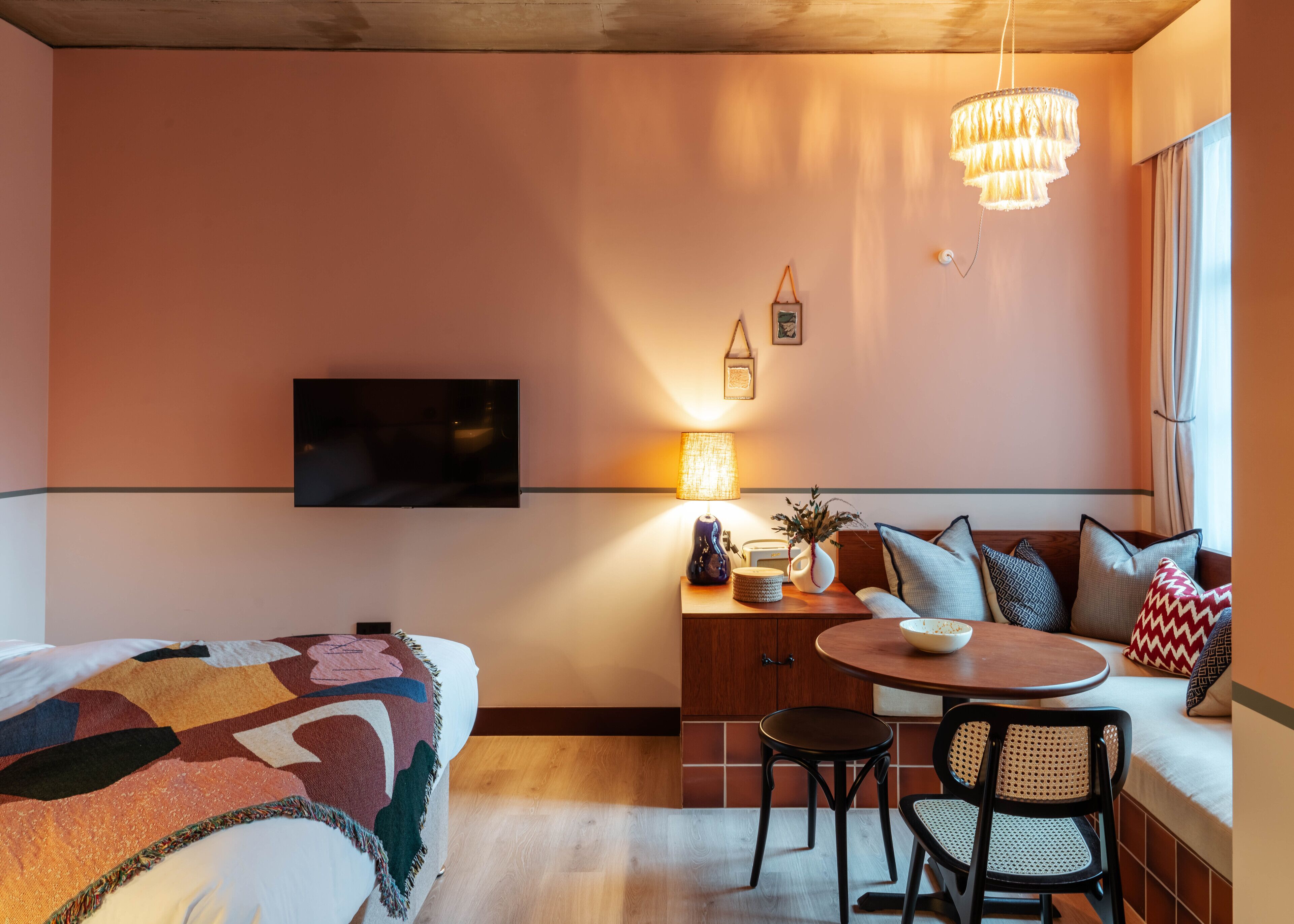 A cozy room with a bed, a desk with a lamp, a TV, and a dining area with chairs and a table.
