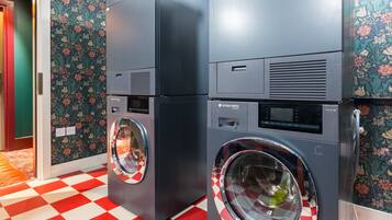 A laundry facility with two front-loading machines, a red and white checkered floor, and floral wallpaper.