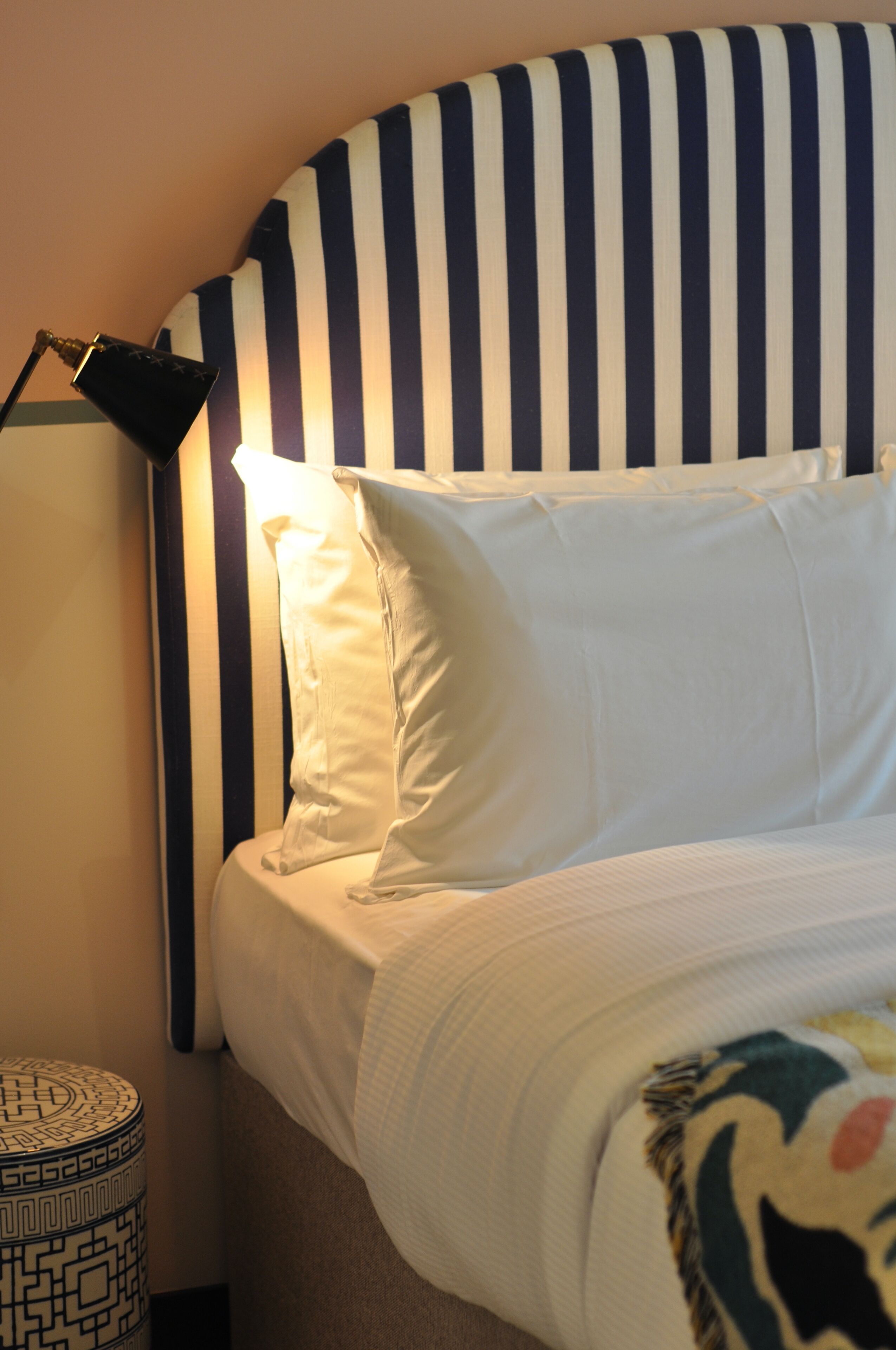 A bed with striped headboard, white pillows, and a patterned side table.