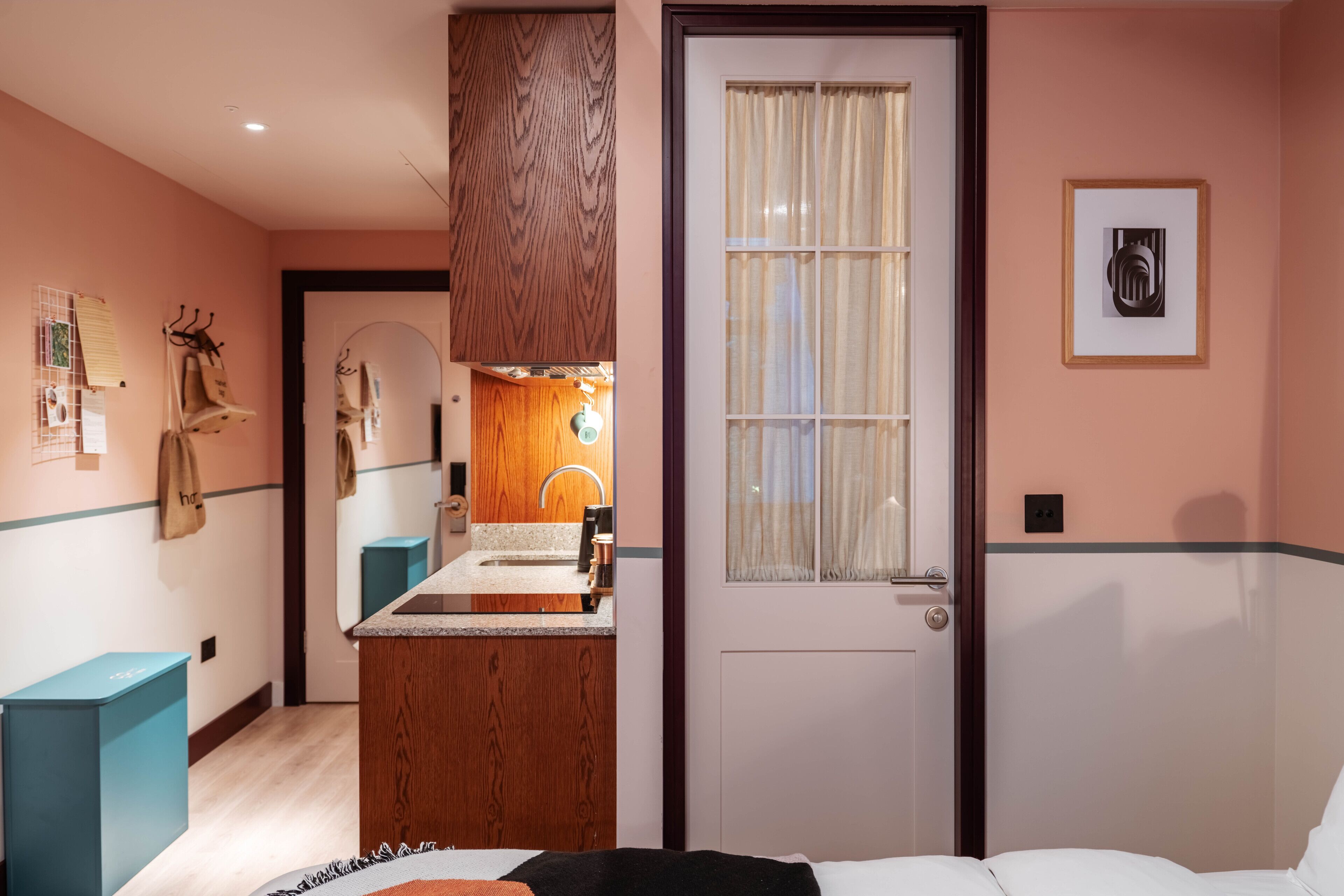 A hotel room with a wooden vanity, a bed, a door with a window, and a framed picture on the wall.