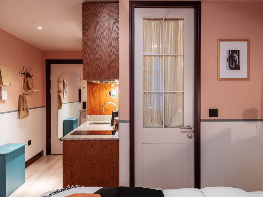 A hotel room with a wooden vanity, a bed, a door with a window, and a framed picture on the wall.