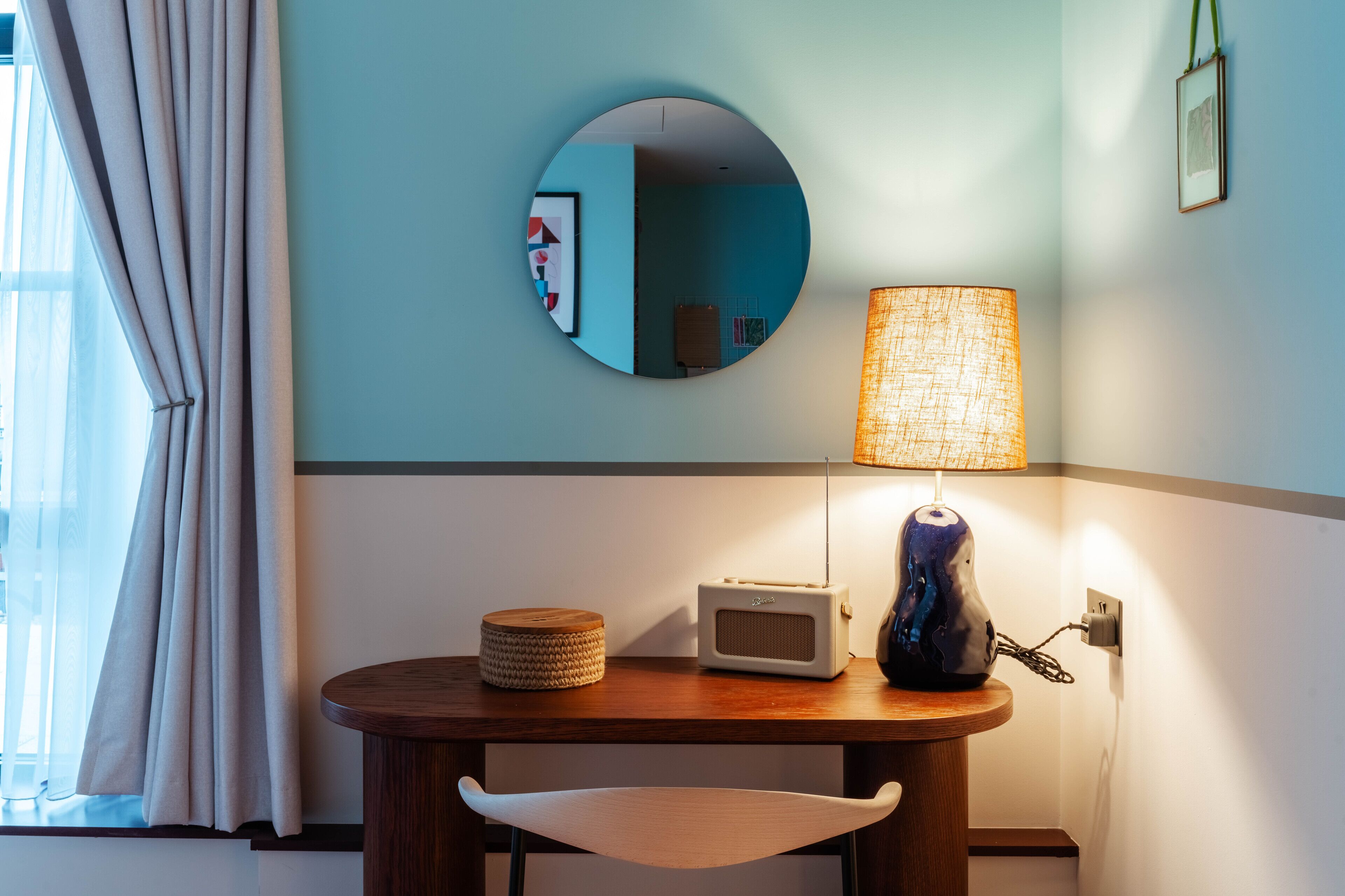 A room with a round mirror, a lamp, a radio, and a chair.