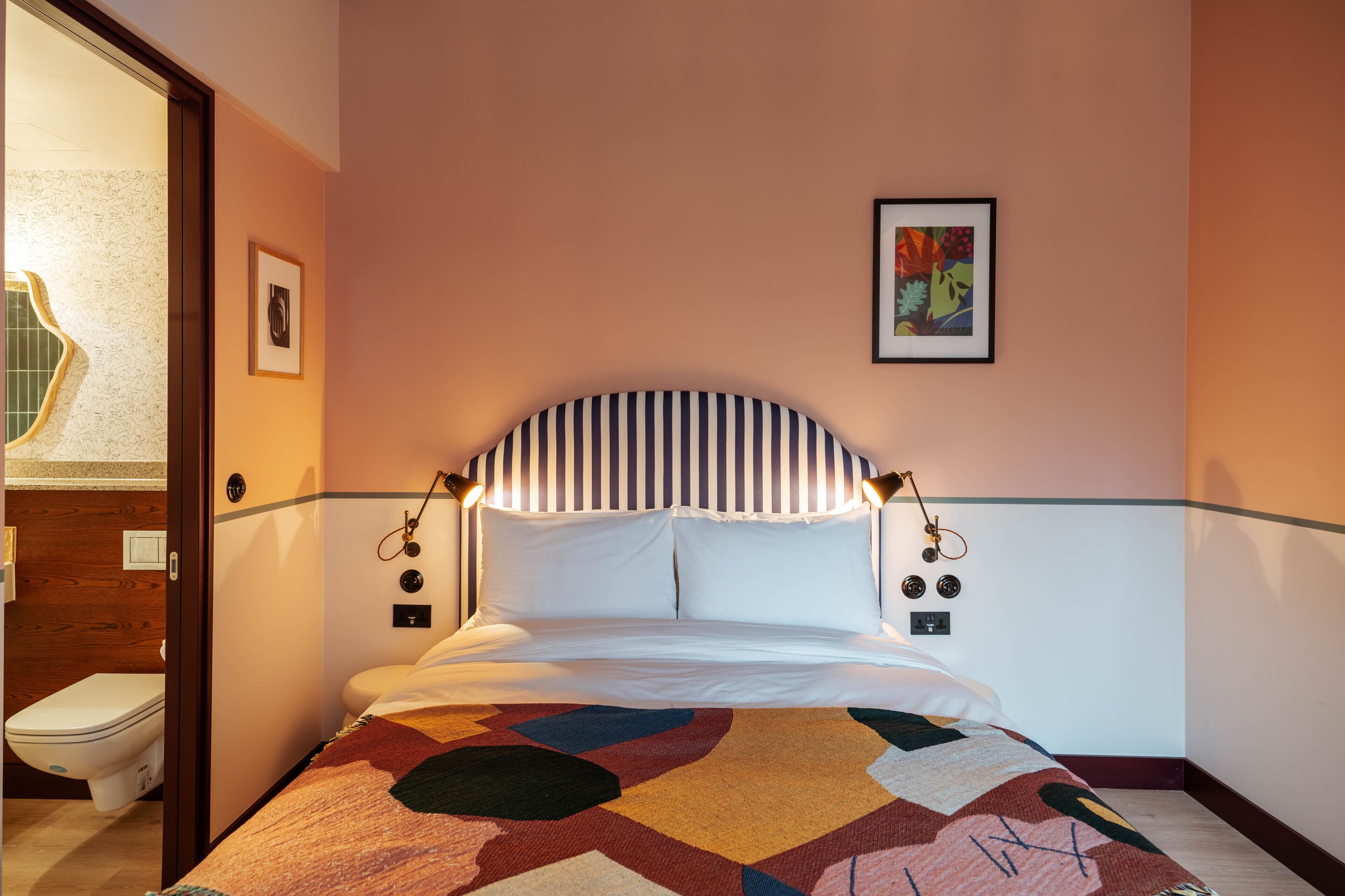 Ein Schlafzimmer mit einem gestreiften Kopfteil, einer farbenfrohen Steudecke und einem gerahmten Kunstwerk an der Wand.