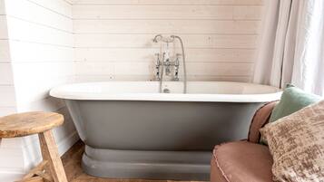 A bathroom with a freestanding bathtub, wooden floor, and a wooden stool.