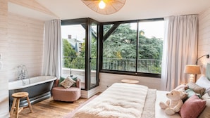 A bedroom with a large window, a bathtub, a bed, and a bedside lamp. - Hôtel SOCLO (Toulouse)