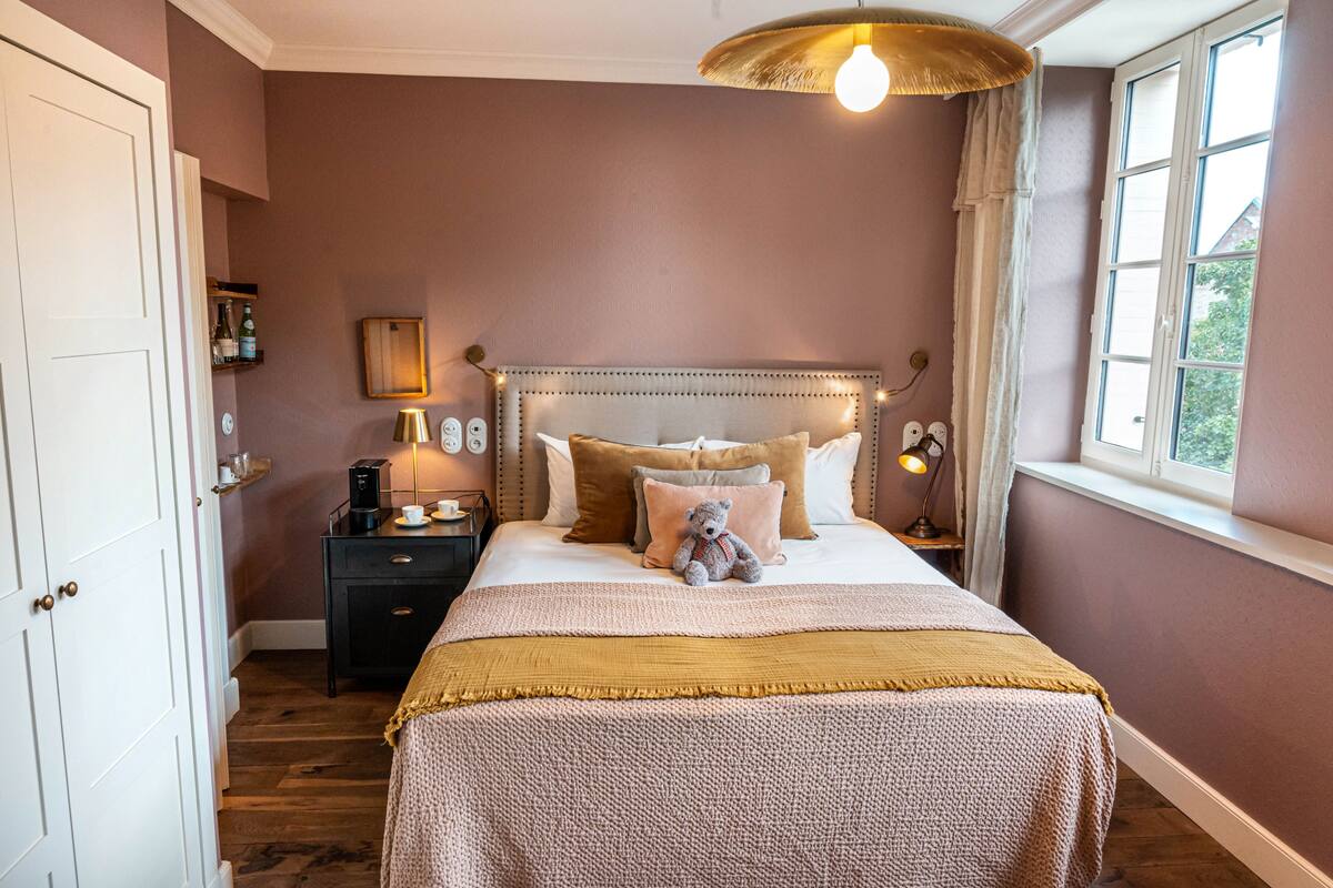 A bedroom with a bed, bedside tables, a nightstand, a window, and a door.