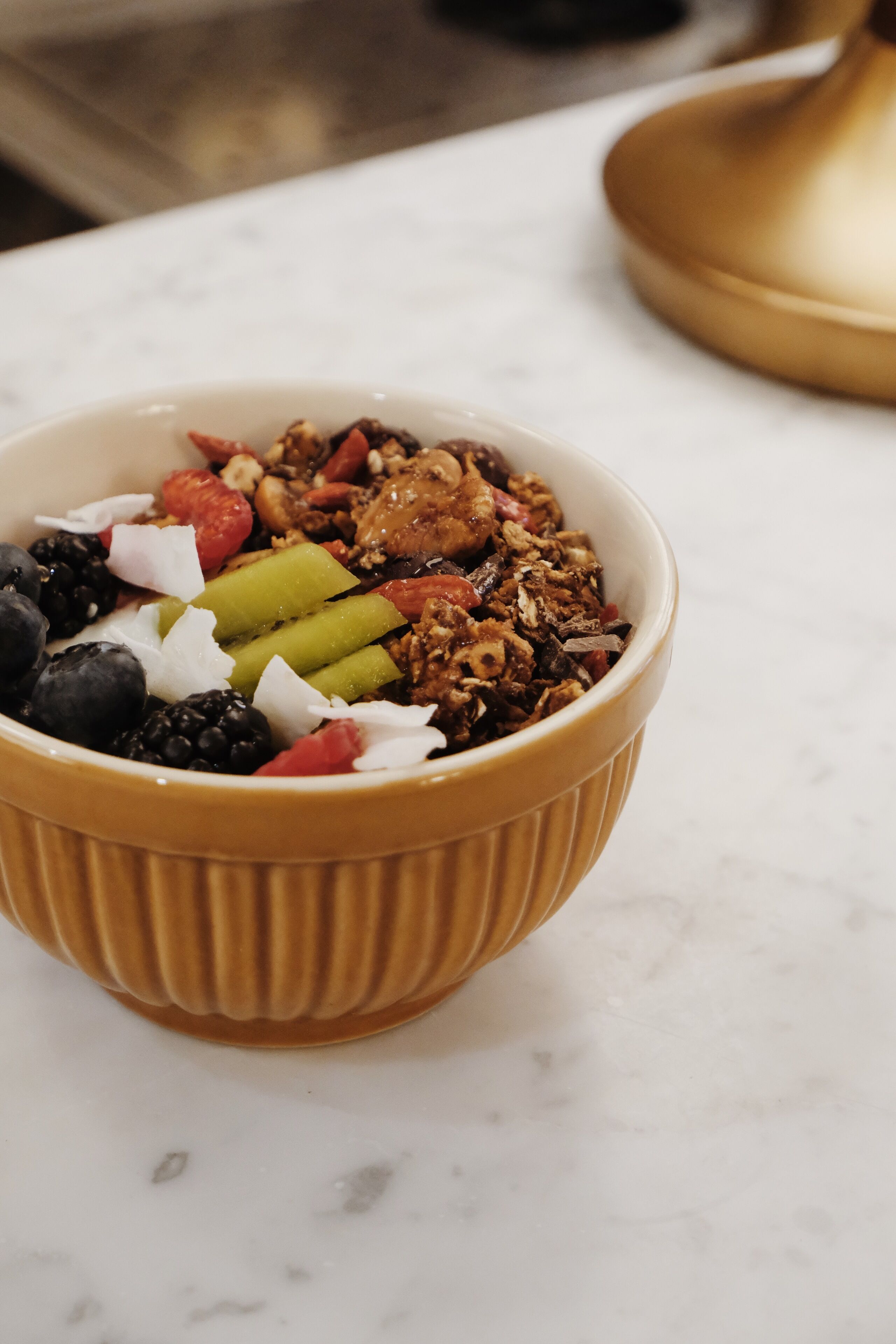 A bowl of granola with mixed fruits and nuts on a marble surface.