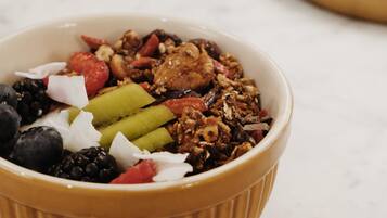 A bowl of granola with mixed fruits and nuts on a marble surface.
