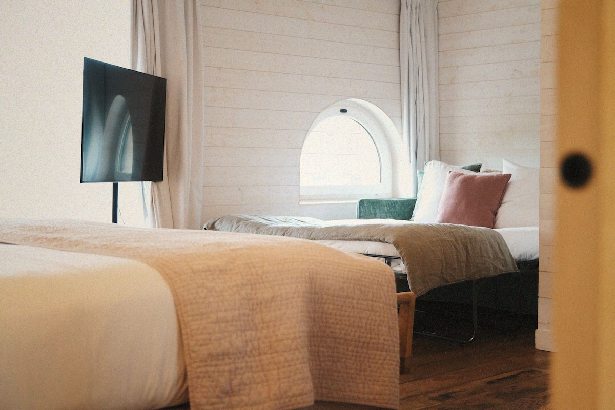 A bedroom with two beds, a TV, a window, and curtains.
