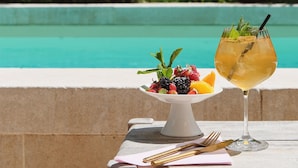 A table with a fruit platter and a cocktail glass by a poolside. - Hôtel SOCLO (Toulouse)