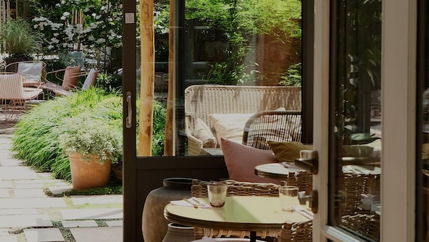 An outdoor seating area with wicker furniture and a table, surrounded by potted plants and a stone pathway. - Hôtel SOCLO (Toulouse)