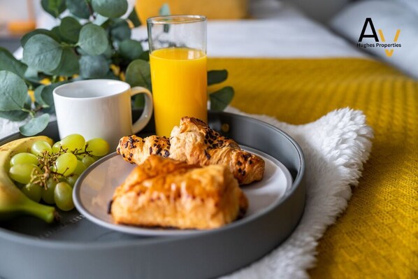 Une table dressée pour le petit-déjeuner avec des croissants, des raisins, un verre de jus d’orange et une tasse blanche posée sur une assiette.