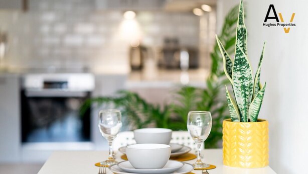 A dining table set with white bowls, gold plates, and wine glasses, with a yellow vase containing a plant.