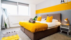 A modern bedroom with a large bed, a nightstand, a lamp, and a window.