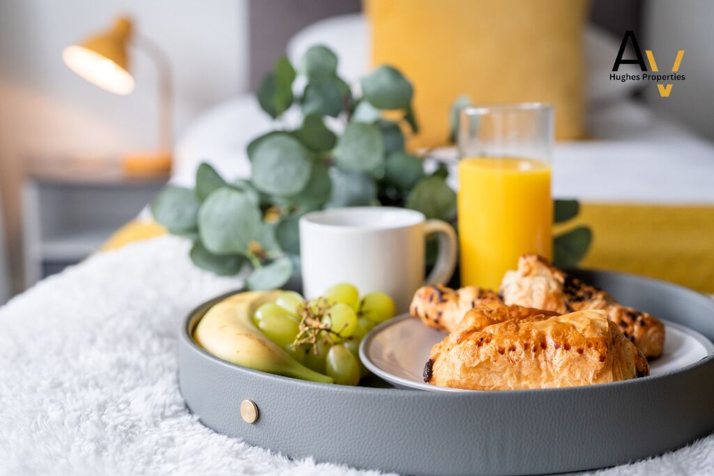 Una bandeja de desayuno con una taza, un vaso de jugo de naranja, un plato con huevos, uvas y pasteles sobre una manta blanca y esponjosa.