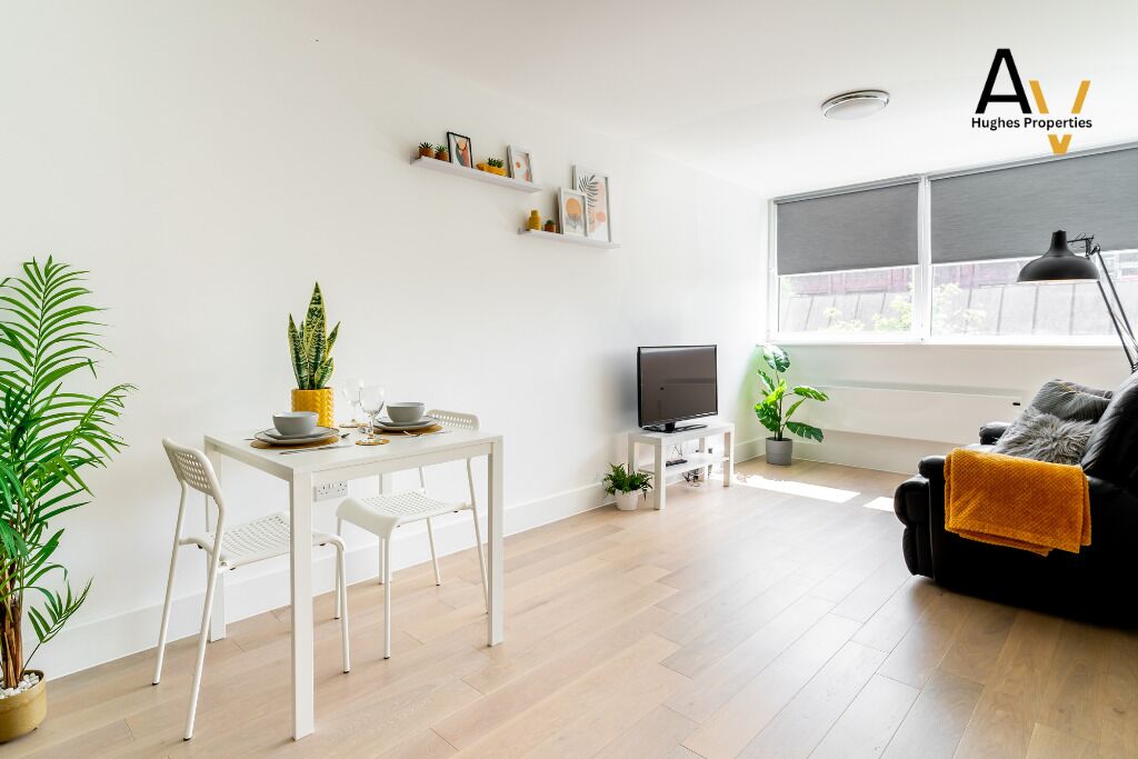 Un salon moderne comprenant une table à manger, des chaises, un téléviseur et un canapé. Des plantes et des œuvres d’art ornent les étagères.