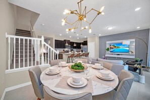 A modern dining area with a round table set for six, a staircase, and a kitchen in the background. - Elegant Townhome, Private Splash Pool, Near Theme Parks! (Davenport)