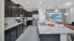 A modern kitchen with dark cabinets, a granite countertop, stainless steel appliances, and a dining area with a marble island. - Elegant Townhome, Private Splash Pool, Near Theme Parks! (Davenport)