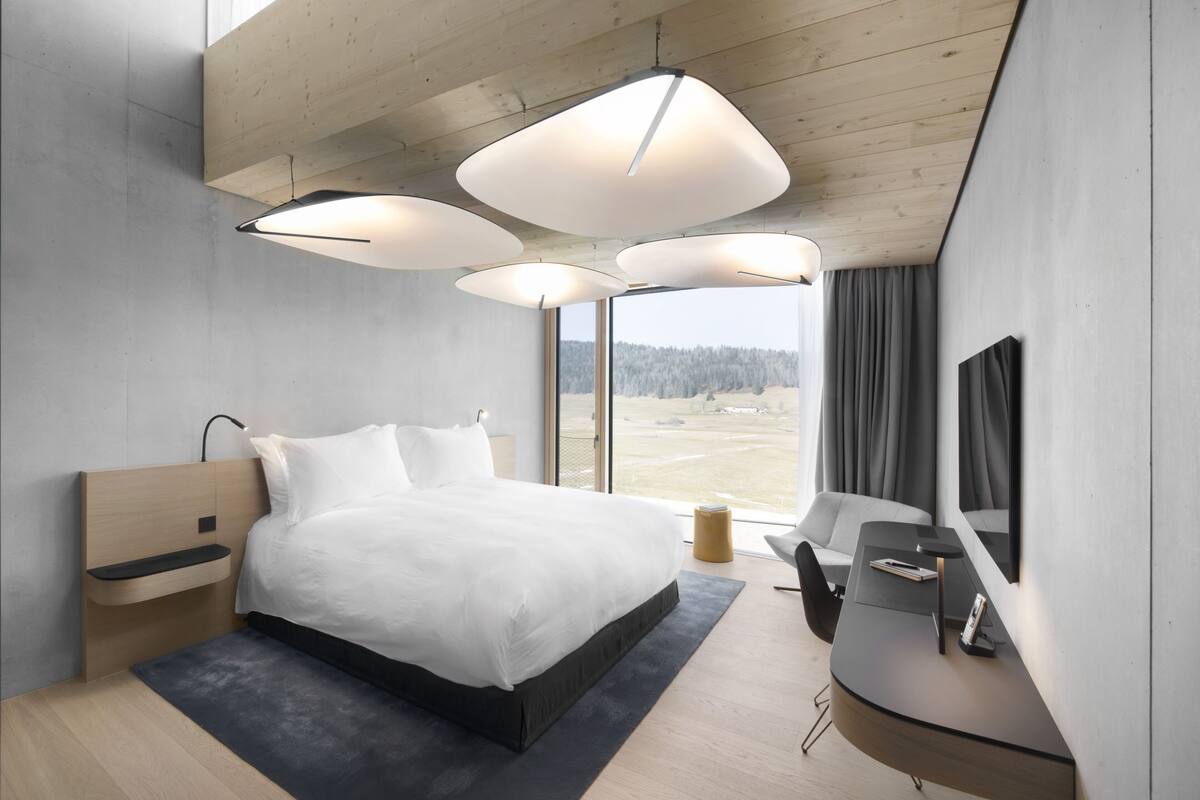 A modern bedroom with a large bed, a desk, and a TV. There are three pendant lights above the bed.