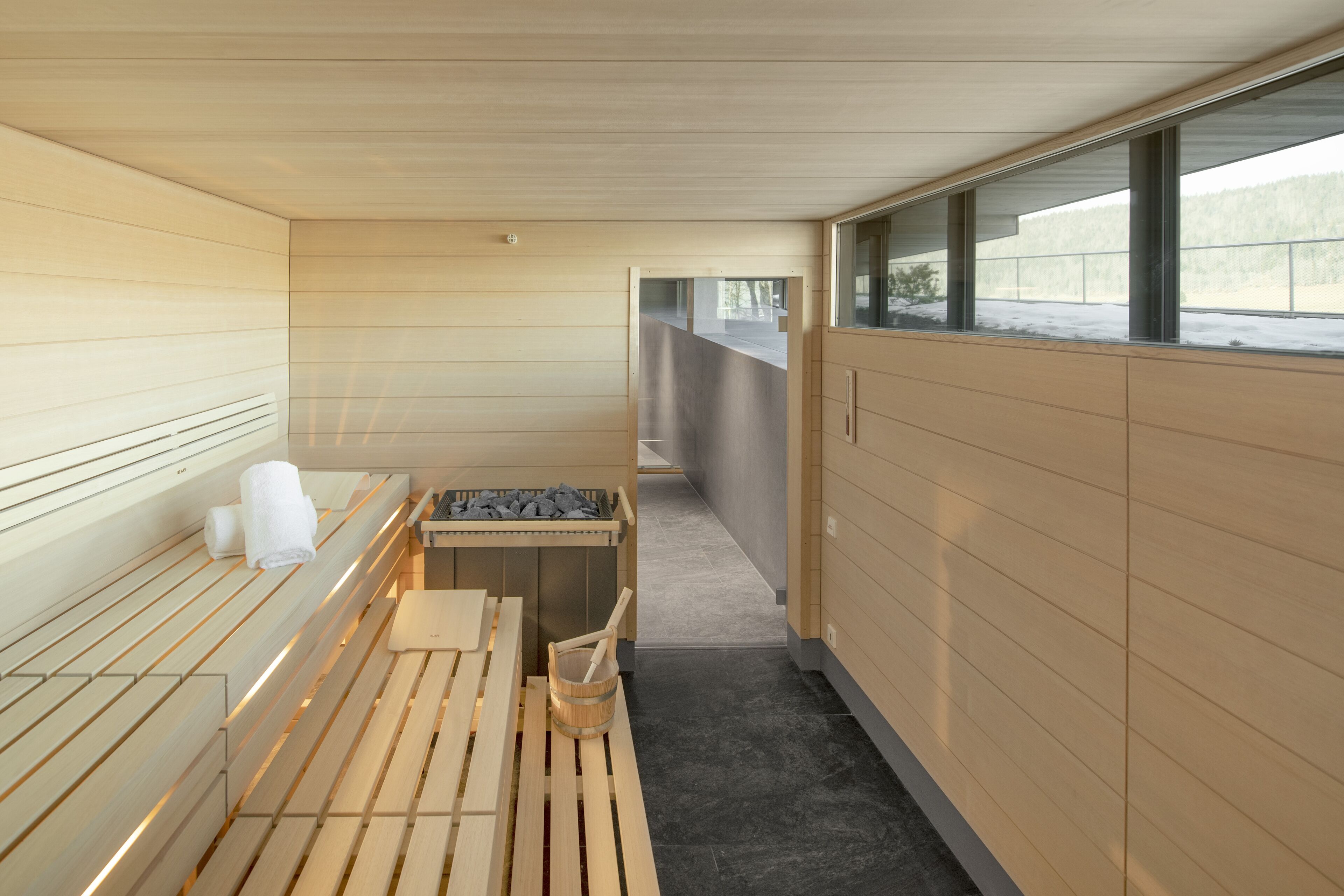 A sauna room with wooden benches, a bench with a towel, a bucket, and a table with stones.