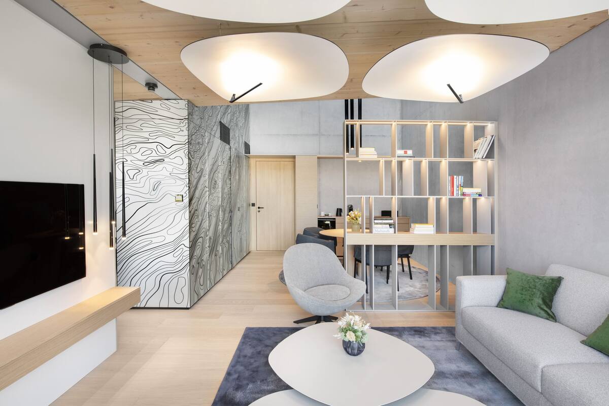 A modern living room with a flat-screen TV, a grey sofa, a white coffee table, and a bookshelf.
