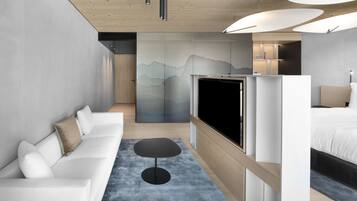 Een moderne hotelkamer met een witte bank, een klein rond tafeltje, een flatscreen televisie en een bed met houten hoofdbord.
