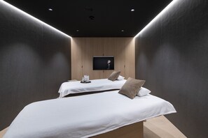 A modern hotel room with two beds, a flat-screen TV mounted on the wall, and a small table with toiletries. - Hôtel des Horlogers (Le Chenit)