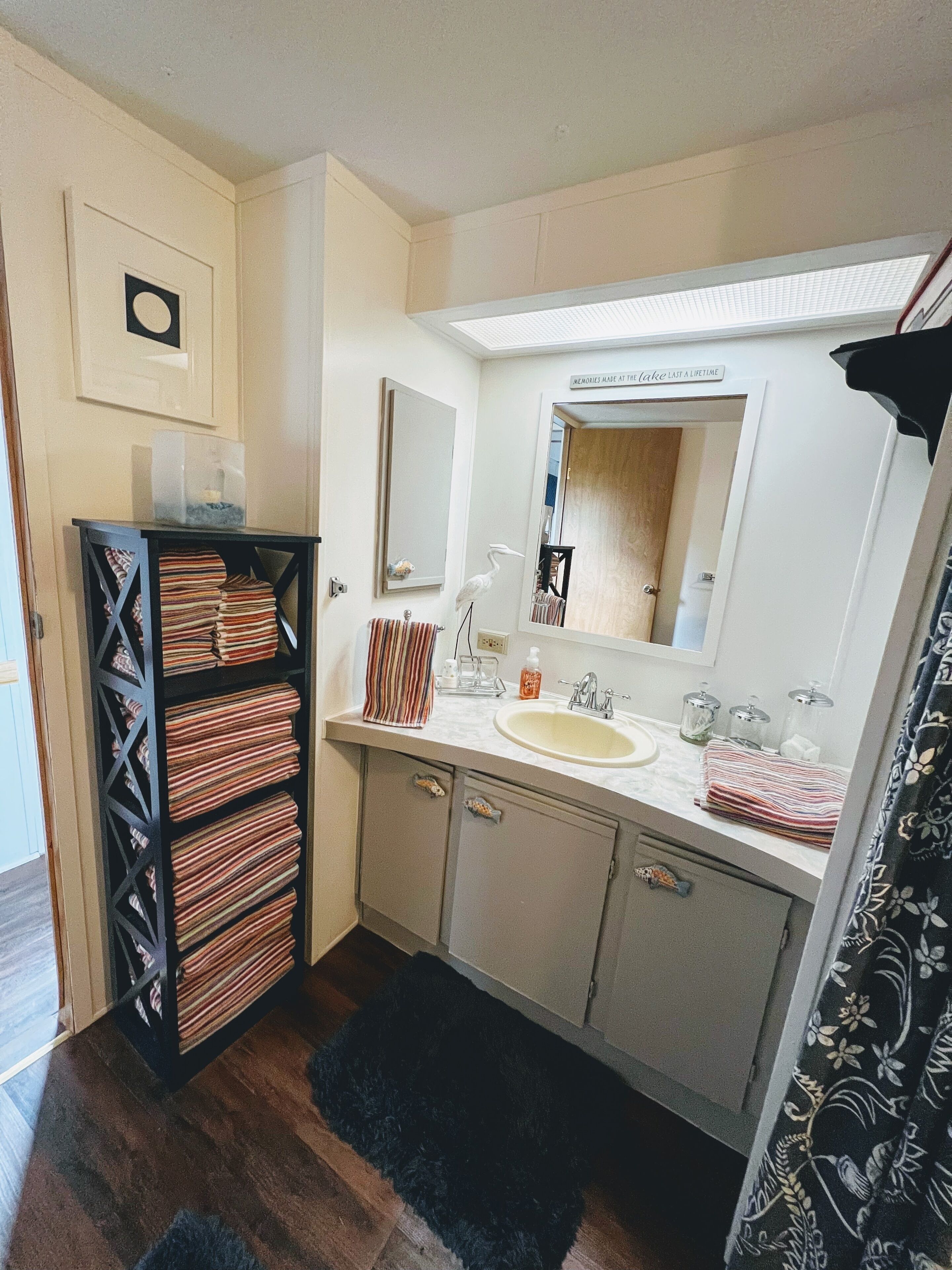 Une salle de bain avec un lavabo, un miroir et un meuble de rangement noir contenant des serviettes.