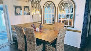 A dining area with a wooden table, wicker chairs, and arched windows.