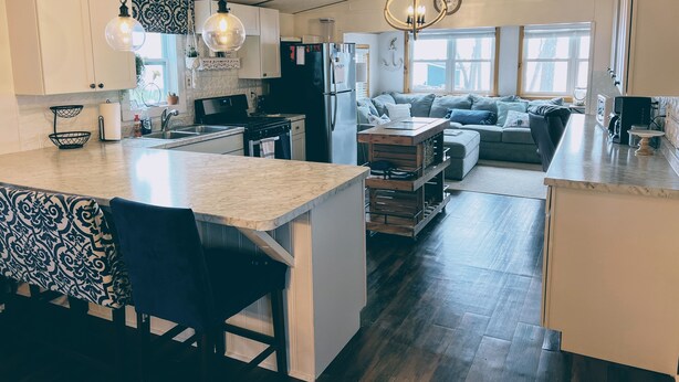 A modern kitchen with a central island, a dining area with a patterned tablecloth, and a cozy seating area with a sofa and cushions.