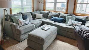 A cozy living room with a sectional sofa, a floor lamp, and a large window with blinds.