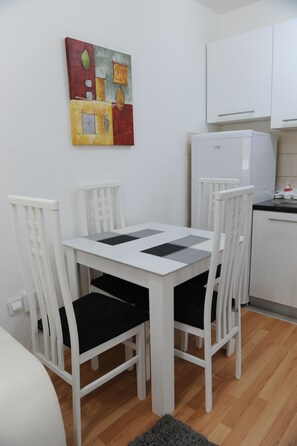 Un petit coin repas blanc, avec une table et quatre chaises, un réfrigérateur et un plan de travail de cuisine.