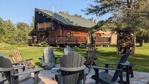 A log cabin with a porch, outdoor seating with Adirondack chairs, and a well-maintained lawn.