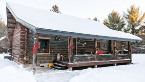 A log cabin with a porch, decorated with red bows, in a snowy setting.