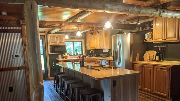 A kitchen with wooden cabinets, a central island with stools, stainless steel appliances, and a herringbone wood floor.