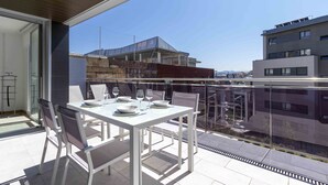 A balcony with a white table set for dining, overlooking a cityscape with buildings and a clear sky.