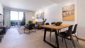 A modern living room with a dining area, a sofa, a lamp, and a painting on the wall.