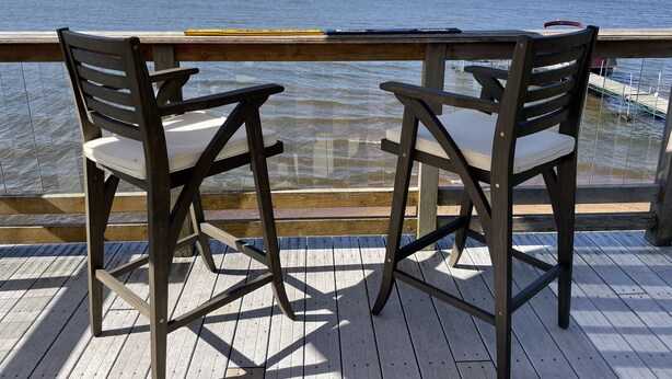Dos sillas de madera con cojines blancos en una terraza de madera con vista al mar.