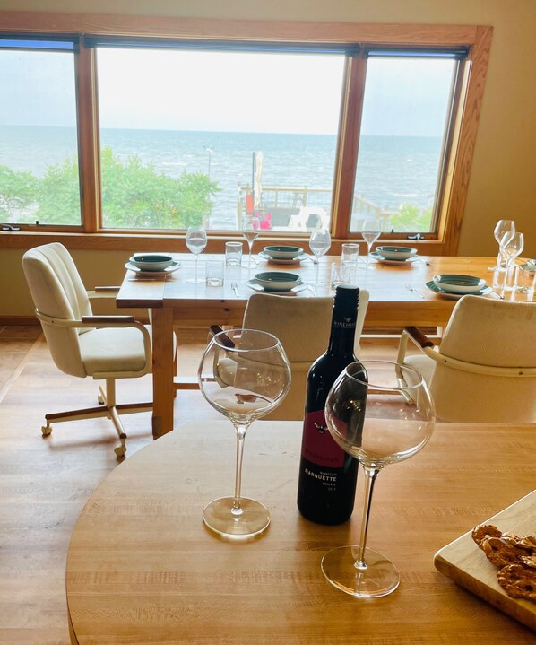Una mesa de comedor dispuesta con copas de vino y una botella, con vistas a un paisaje marino.
