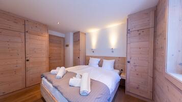 A bedroom with a large bed, wooden wardrobe, and wall-mounted lighting.